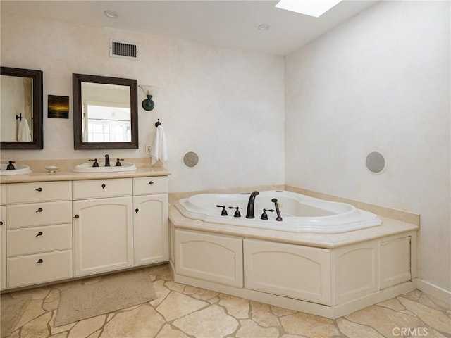 bathroom with a skylight, vanity, a garden tub, and visible vents