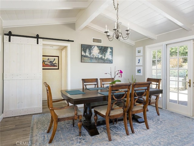 dining space featuring a notable chandelier, lofted ceiling with beams, a barn door, wood finished floors, and visible vents
