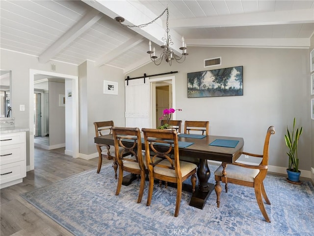 dining room with visible vents, wood finished floors, a barn door, baseboards, and vaulted ceiling with beams