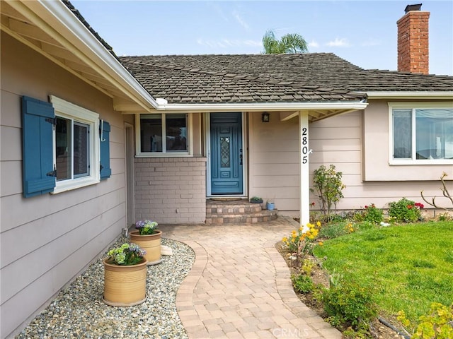 entrance to property featuring a chimney, a yard, and brick siding