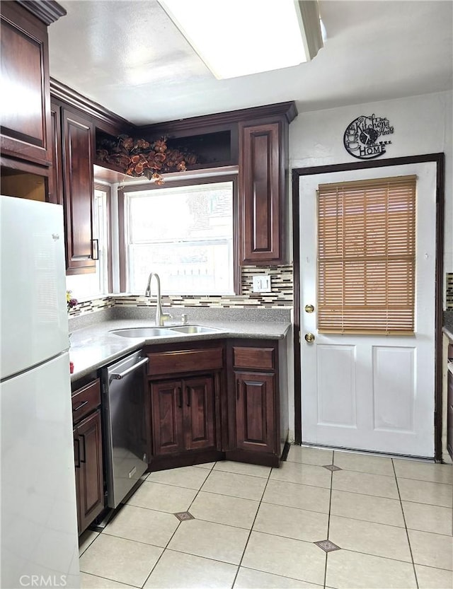 kitchen with stainless steel dishwasher, light tile patterned floors, a sink, and freestanding refrigerator