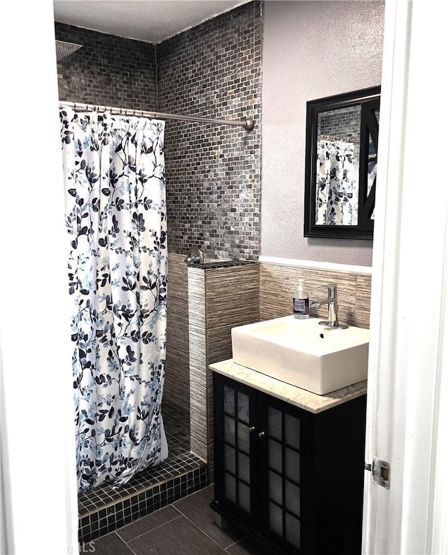bathroom with vanity, tile patterned flooring, a wainscoted wall, tile walls, and a stall shower