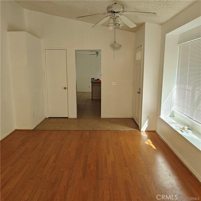 unfurnished room with light wood finished floors, baseboards, a ceiling fan, and a textured ceiling