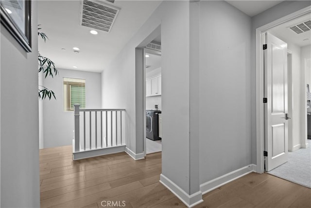 hallway with washer / clothes dryer, visible vents, wood finished floors, and an upstairs landing