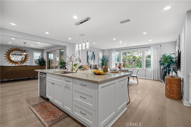 kitchen with a sink, a kitchen island with sink, white cabinetry, stainless steel dishwasher, and visible vents