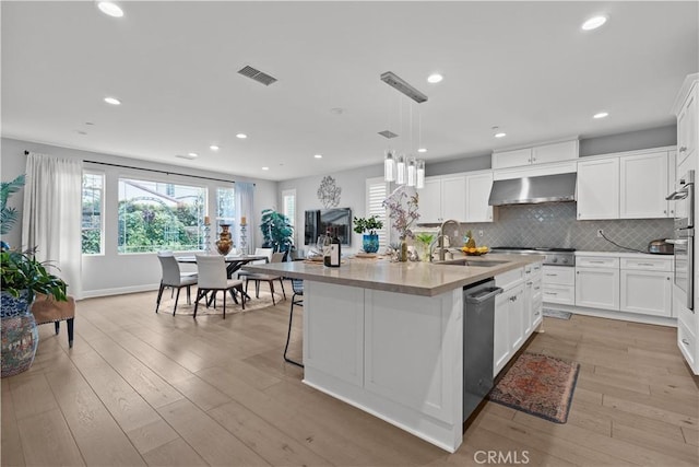 kitchen featuring wall chimney range hood, a sink, light wood finished floors, stainless steel appliances, and white cabinetry