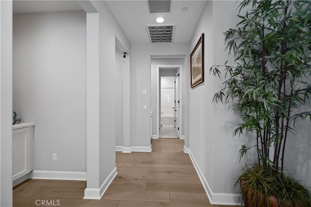 hallway with baseboards, visible vents, and light wood-style flooring