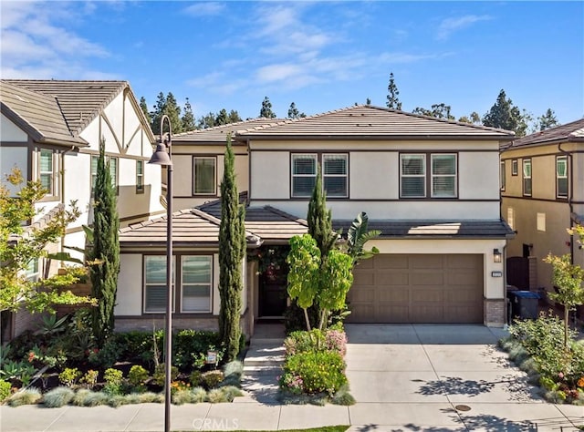 tudor-style house with a tiled roof, an attached garage, driveway, and stucco siding