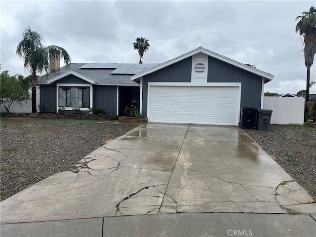 ranch-style home featuring roof mounted solar panels, a garage, fence, a shingled roof, and driveway