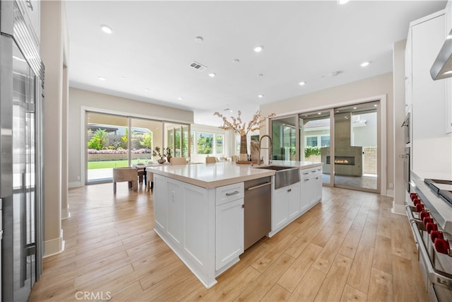 kitchen with a warm lit fireplace, a center island with sink, visible vents, appliances with stainless steel finishes, and a sink