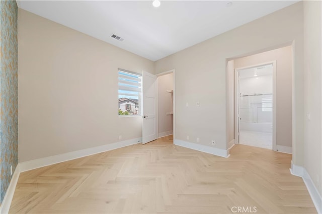 unfurnished bedroom featuring visible vents, baseboards, ensuite bathroom, a walk in closet, and wallpapered walls