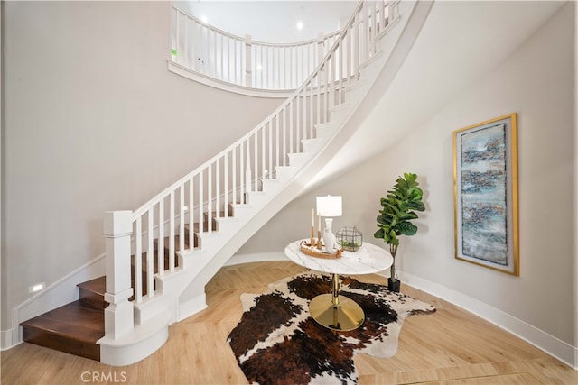 stairway featuring a high ceiling, baseboards, and wood finished floors