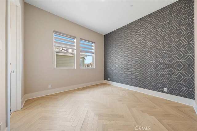 unfurnished room with an accent wall and baseboards