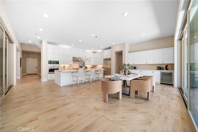 kitchen featuring a kitchen bar, white cabinets, a large island, wine cooler, and built in appliances