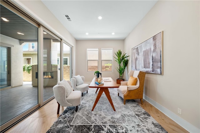 sitting room with light wood-style floors, a glass covered fireplace, visible vents, recessed lighting, and baseboards