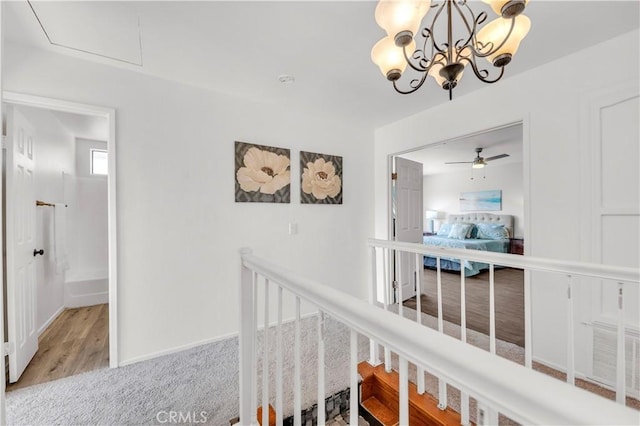 hall with baseboards, an upstairs landing, wood finished floors, and an inviting chandelier