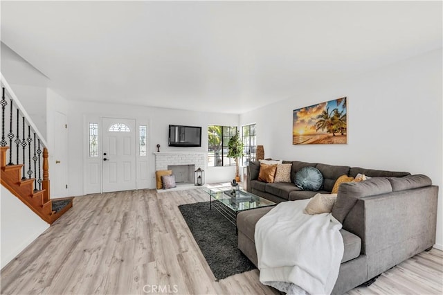 living area with baseboards, light wood-style flooring, a brick fireplace, and stairway