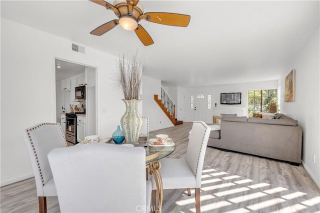 dining area featuring visible vents, baseboards, stairway, a ceiling fan, and light wood-style flooring