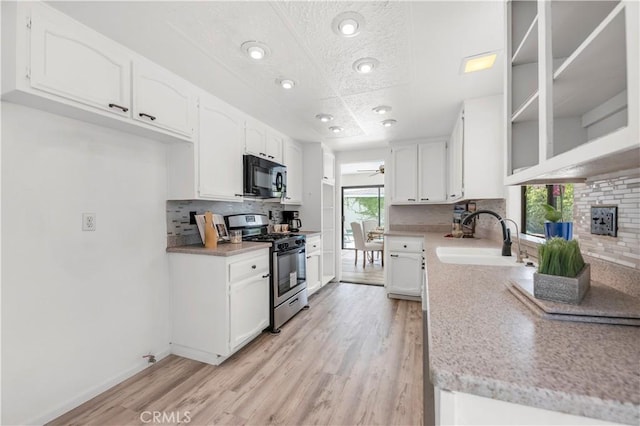 kitchen featuring decorative backsplash, black microwave, stainless steel gas range oven, a sink, and light wood finished floors