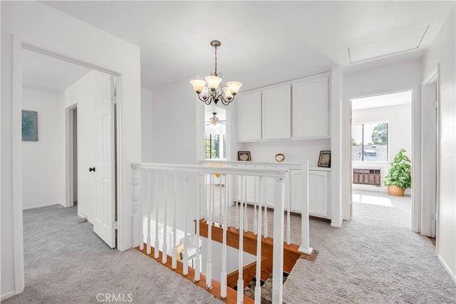 hall with light colored carpet, baseboards, an upstairs landing, and an inviting chandelier