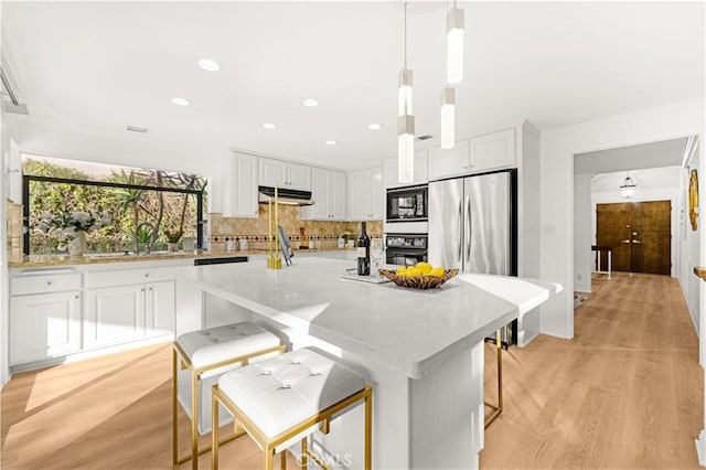 19 Alameda, Irvine, CA 92620 - kitchen with white cabinets, light wood finished floors, under cabinet range hood, decorative backsplash, and black appliances