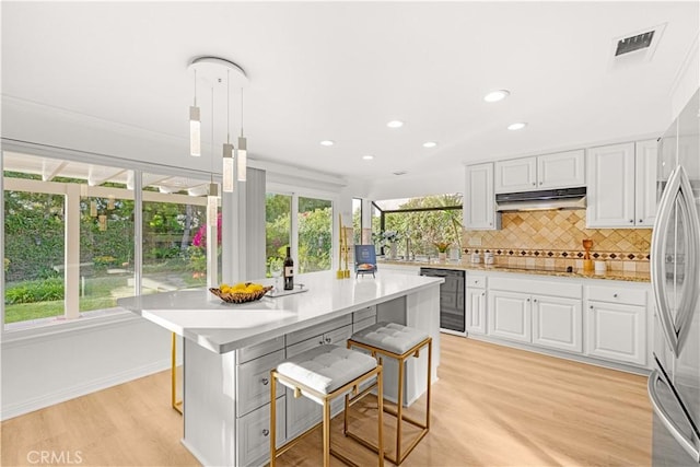 19 Alameda, Irvine, CA 92620 - kitchen with a breakfast bar, light wood-type flooring, backsplash, under cabinet range hood, and visible vents