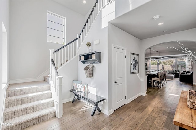 staircase with arched walkways, hardwood / wood-style floors, baseboards, and recessed lighting
