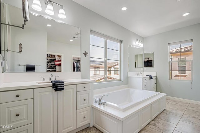 full bath featuring a sink, a spacious closet, recessed lighting, two vanities, and a garden tub