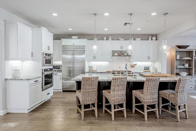 kitchen featuring tasteful backsplash, white cabinets, appliances with stainless steel finishes, under cabinet range hood, and light wood-style flooring