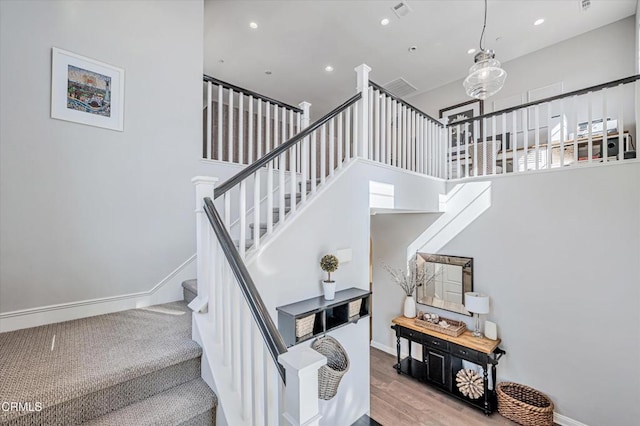 stairs with a towering ceiling, baseboards, recessed lighting, visible vents, and wood finished floors