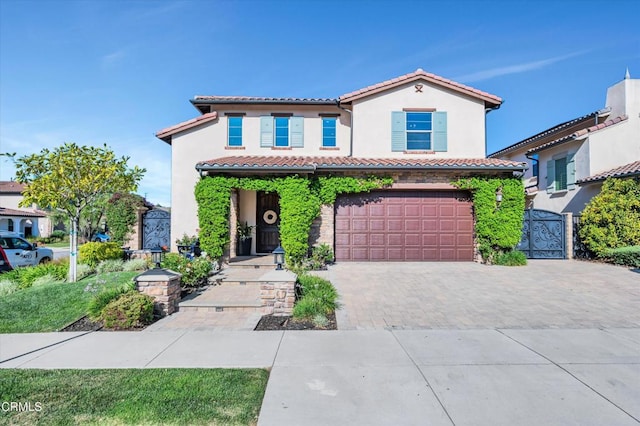 mediterranean / spanish-style house with a garage, a tile roof, stucco siding, a gate, and decorative driveway