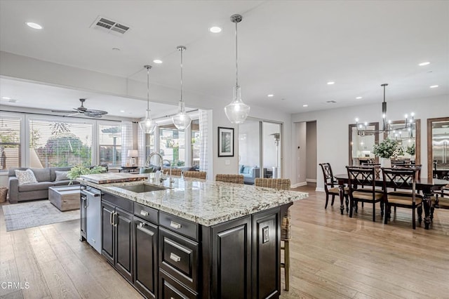 kitchen featuring visible vents, a sink, open floor plan, a kitchen island with sink, and light wood finished floors