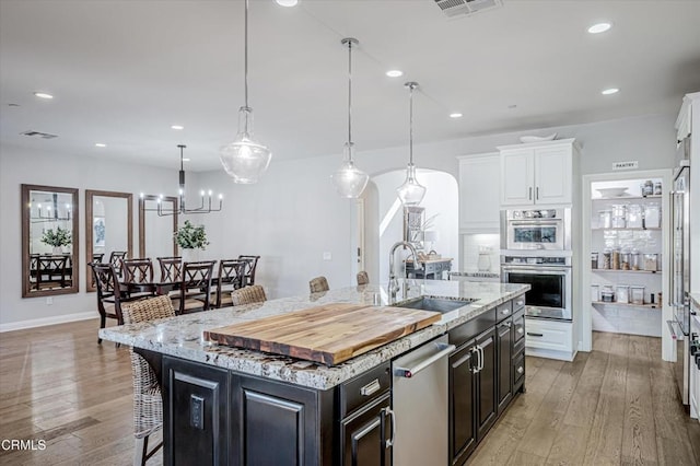 kitchen with white cabinetry, appliances with stainless steel finishes, a sink, a center island with sink, and a breakfast bar area