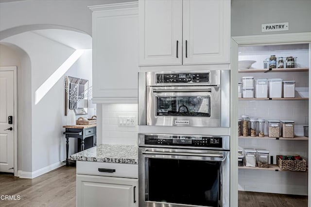 kitchen featuring arched walkways, stainless steel double oven, decorative backsplash, and wood finished floors