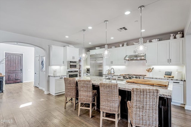 kitchen with under cabinet range hood, visible vents, arched walkways, stainless steel built in fridge, and a sink