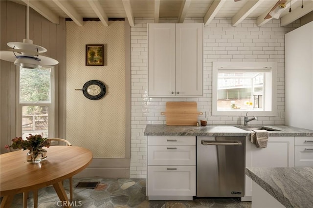 kitchen featuring white cabinetry, stone finish floor, beam ceiling, dishwasher, and a sink