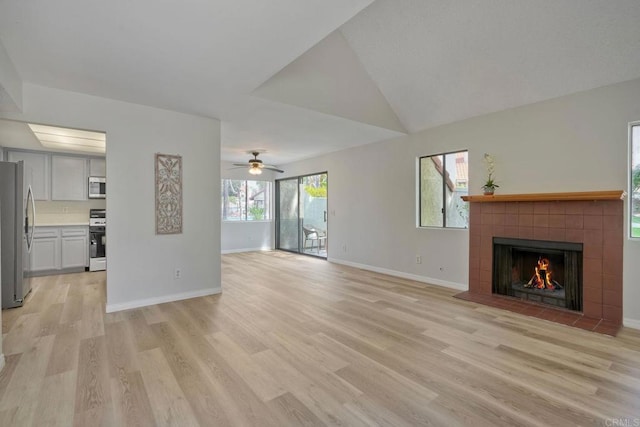 321 N Melrose Dr Unit A, Vista, CA 92083 - unfurnished living room featuring light wood-style floors, a ceiling fan, a tiled fireplace, lofted ceiling, and baseboards