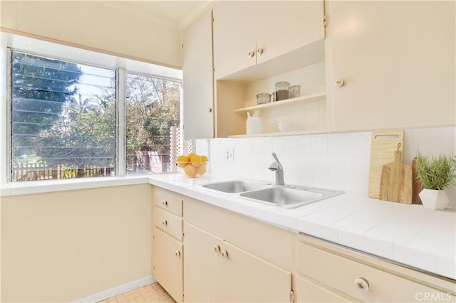 kitchen featuring baseboards, ornamental molding, tile counters, backsplash, and a sink