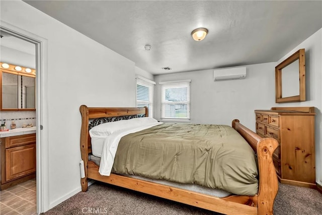 bedroom with a wall mounted air conditioner, baseboards, visible vents, and ensuite bath