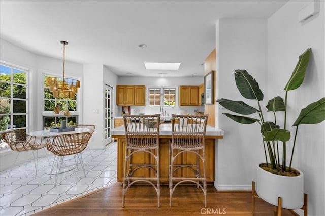 2824 Westwood Blvd, Los Angeles, CA 90064 - kitchen featuring light countertops, a peninsula, brown cabinets, pendant lighting, and a skylight