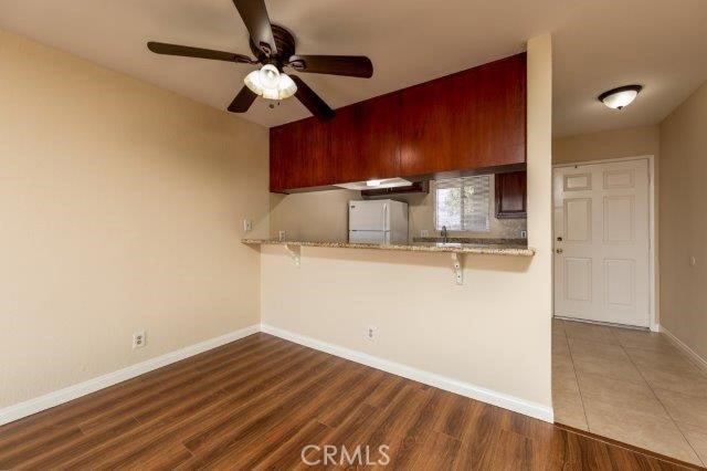 kitchen with baseboards, freestanding refrigerator, a kitchen bar, ceiling fan, and wood finished floors