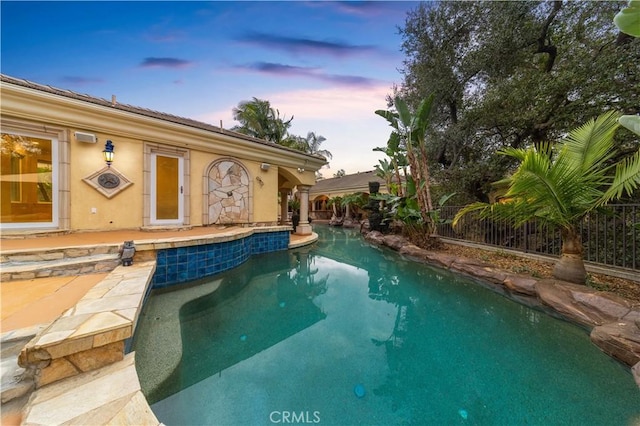 pool at dusk featuring an outdoor pool, a patio, and fence