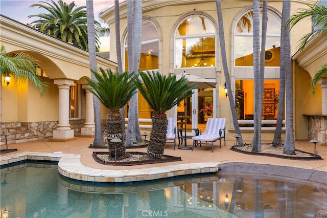 pool at dusk with an outdoor pool, french doors, and a patio area