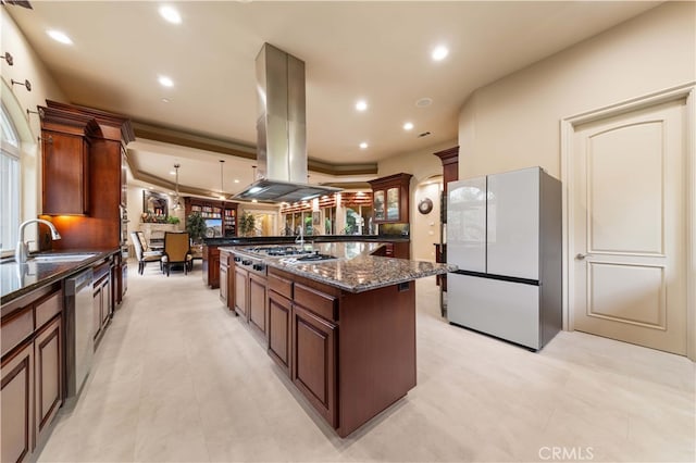 kitchen with dark stone countertops, stainless steel appliances, a spacious island, island range hood, and a sink