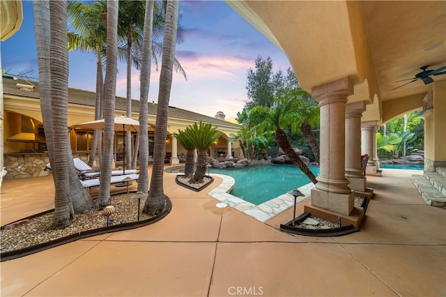 pool at dusk with an outdoor pool, a patio area, and ceiling fan