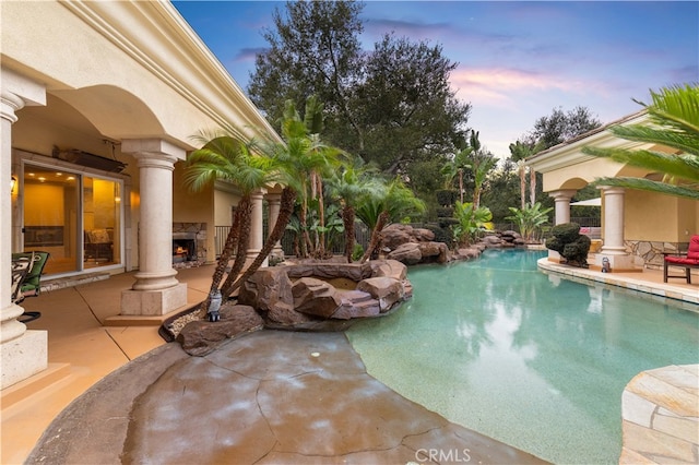 outdoor pool featuring a patio and a warm lit fireplace