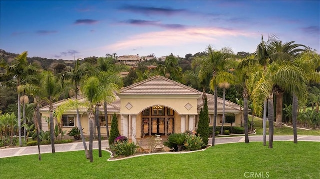 mediterranean / spanish-style home featuring a tiled roof, french doors, stucco siding, and a lawn