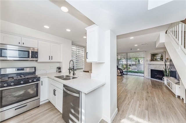 kitchen featuring open floor plan, white cabinetry, light wood-style floors, stainless steel appliances, and a sink