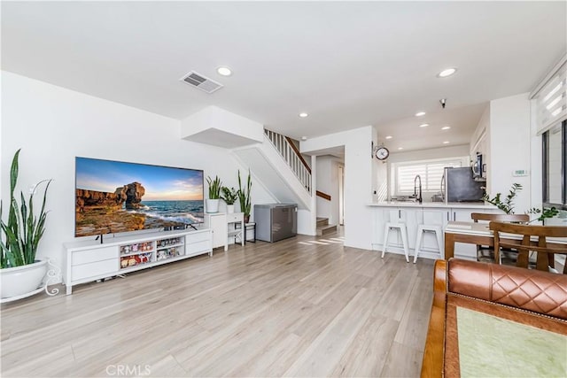living area featuring visible vents, light wood-type flooring, recessed lighting, and stairs