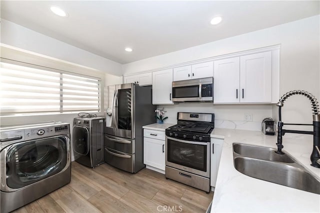 kitchen featuring a sink, light wood-style floors, white cabinetry, stainless steel appliances, and washing machine and dryer